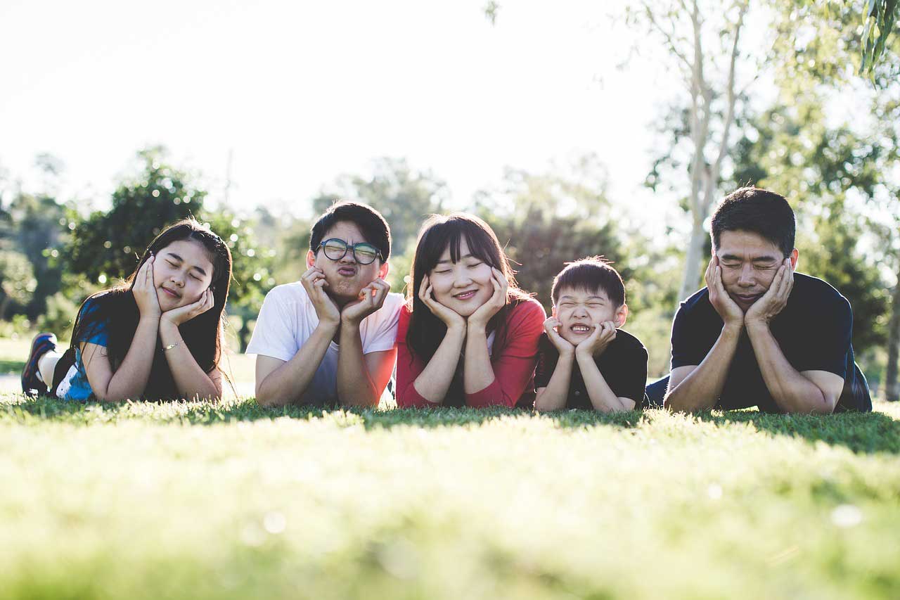 family laying in grass with their hands on chins and smiling or making funny faces