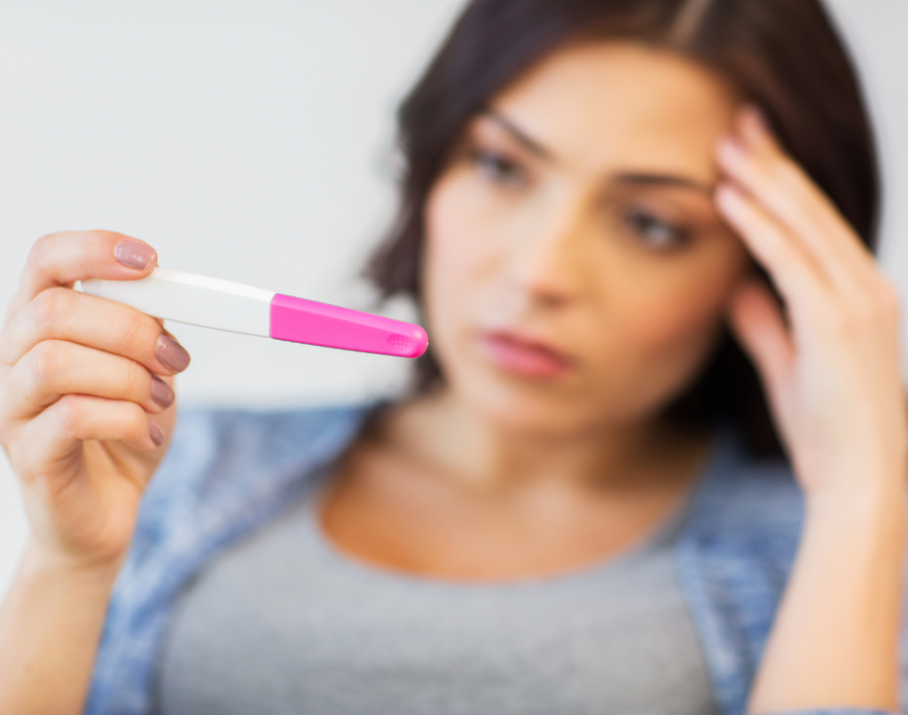 woman looking at pregnancy test with hand to her head